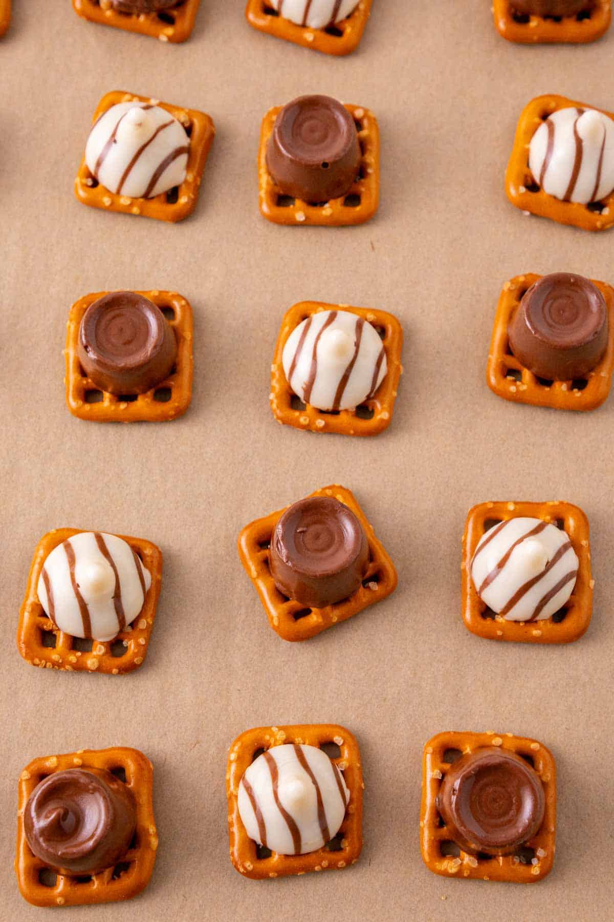 melted rolos and hershey's hugs on top of pretzels on a baking sheet