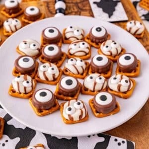 These Halloween Pretzel Rolo Bites are an easy Halloween treat made with crunchy pretzels, gooey Rolo chocolates, Hershey’s Hugs and spooky candy eyes! If you need Easy Halloween Treats, Halloween Pretzel Treats, Halloween Party Food, Halloween Snacks for Kids or quick No Fuss Halloween Desserts, these sweet and salty bites are perfect. They’re ready with just 10 minutes of prep and 3 minutes in the oven, making them a fun choice for Halloween Party Snacks, Classroom Halloween Treats, Halloween Candy Treats and Spooky Halloween Food. Add candy eyeballs to create creepy monster pretzel bites with melted chocolate and caramel. Save these Rolo Pretzel Bites for Halloween Baking Ideas, Easy Halloween Desserts, Kids Halloween Snacks, Halloween Finger Foods and simple Halloween Party Treats everyone will love!
