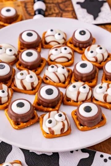 These Halloween Pretzel Rolo Bites are an easy Halloween treat made with crunchy pretzels, gooey Rolo chocolates, Hershey’s Hugs and spooky candy eyes! If you need Easy Halloween Treats, Halloween Pretzel Treats, Halloween Party Food, Halloween Snacks for Kids or quick No Fuss Halloween Desserts, these sweet and salty bites are perfect. They’re ready with just 10 minutes of prep and 3 minutes in the oven, making them a fun choice for Halloween Party Snacks, Classroom Halloween Treats, Halloween Candy Treats and Spooky Halloween Food. Add candy eyeballs to create creepy monster pretzel bites with melted chocolate and caramel. Save these Rolo Pretzel Bites for Halloween Baking Ideas, Easy Halloween Desserts, Kids Halloween Snacks, Halloween Finger Foods and simple Halloween Party Treats everyone will love!