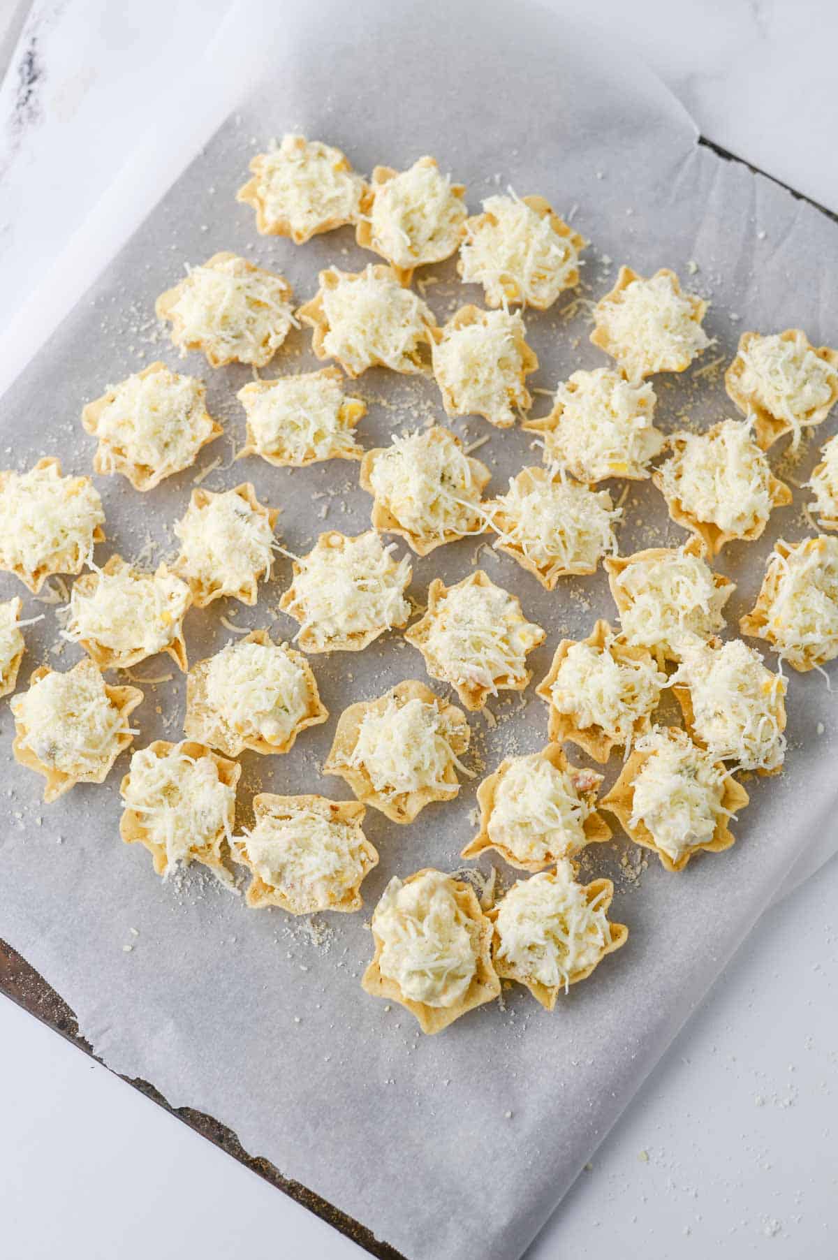 shredded mozzarella on top of cream cheese corn mixture in tostitos scoops on a baking sheet