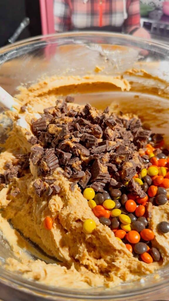 chopped peanut butter cups and mini reese's pieces added to bowl with peanut butter mixture