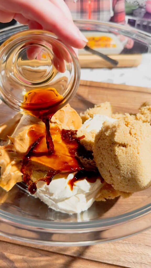 vanlla extract being added to bowl with brown sugar, peanut butter and cream cheese