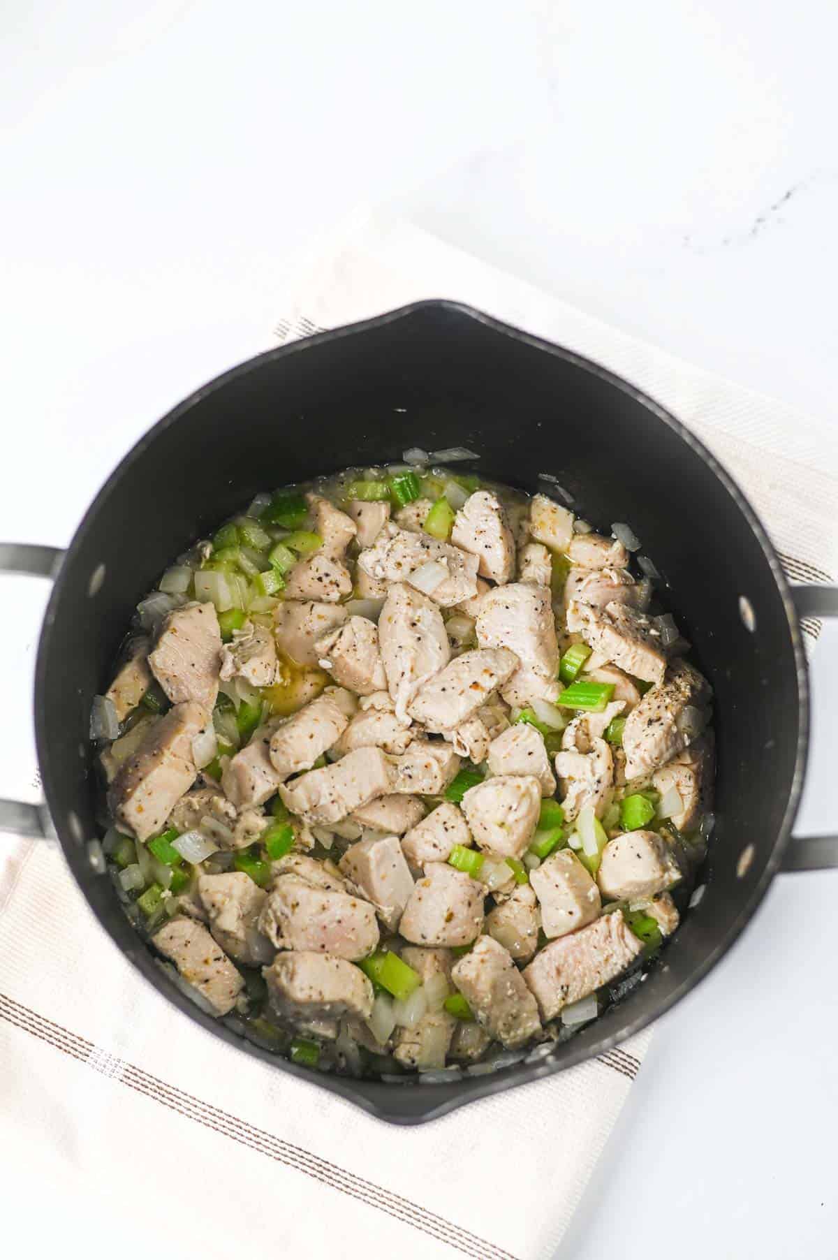 cooked chicken breast pieces, onion and celery in a soup pot