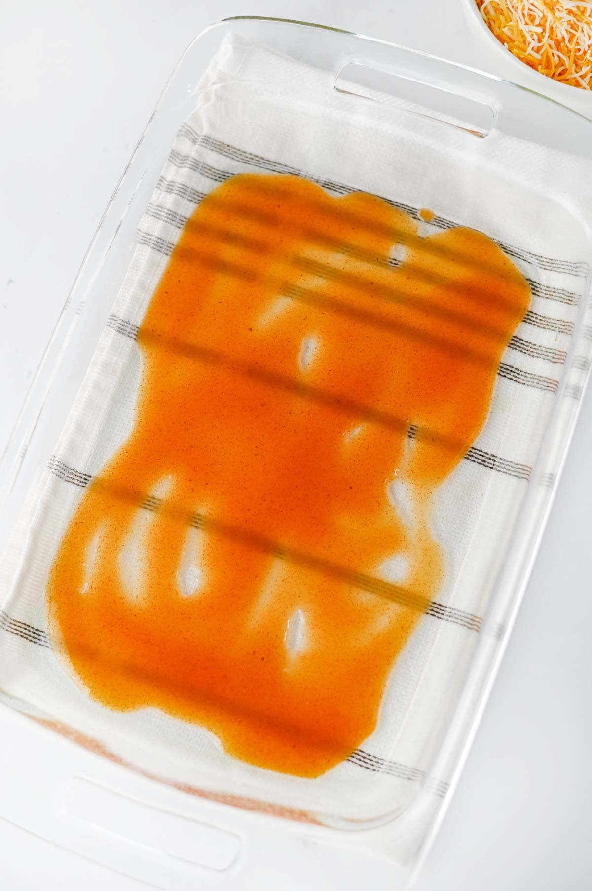 red enchilada sauce in the bottom of a baking dish