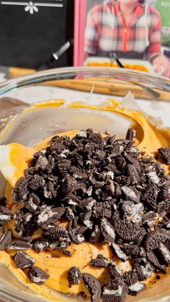 crumbled oreo cookies added to bowl with creamy peanut butter fudge mixture