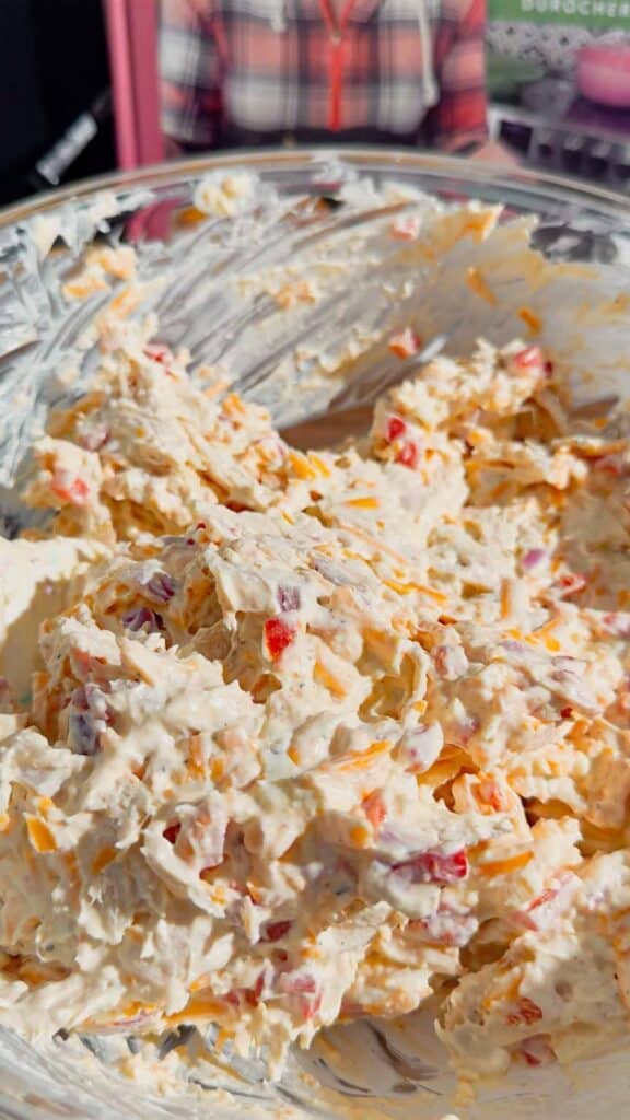 pimento cheese chicken salad mixture being stirred in a glass mixing bowl