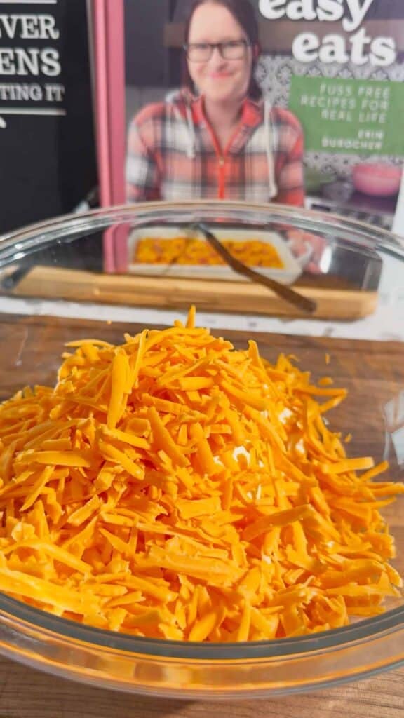 shredded cheddar cheese on top of cream cheese and mayo in a glass mixing bowl