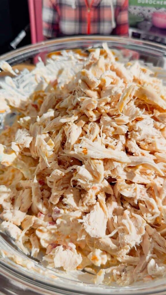 shredded chicken on top of pimento cheese mixture in a glass bowl