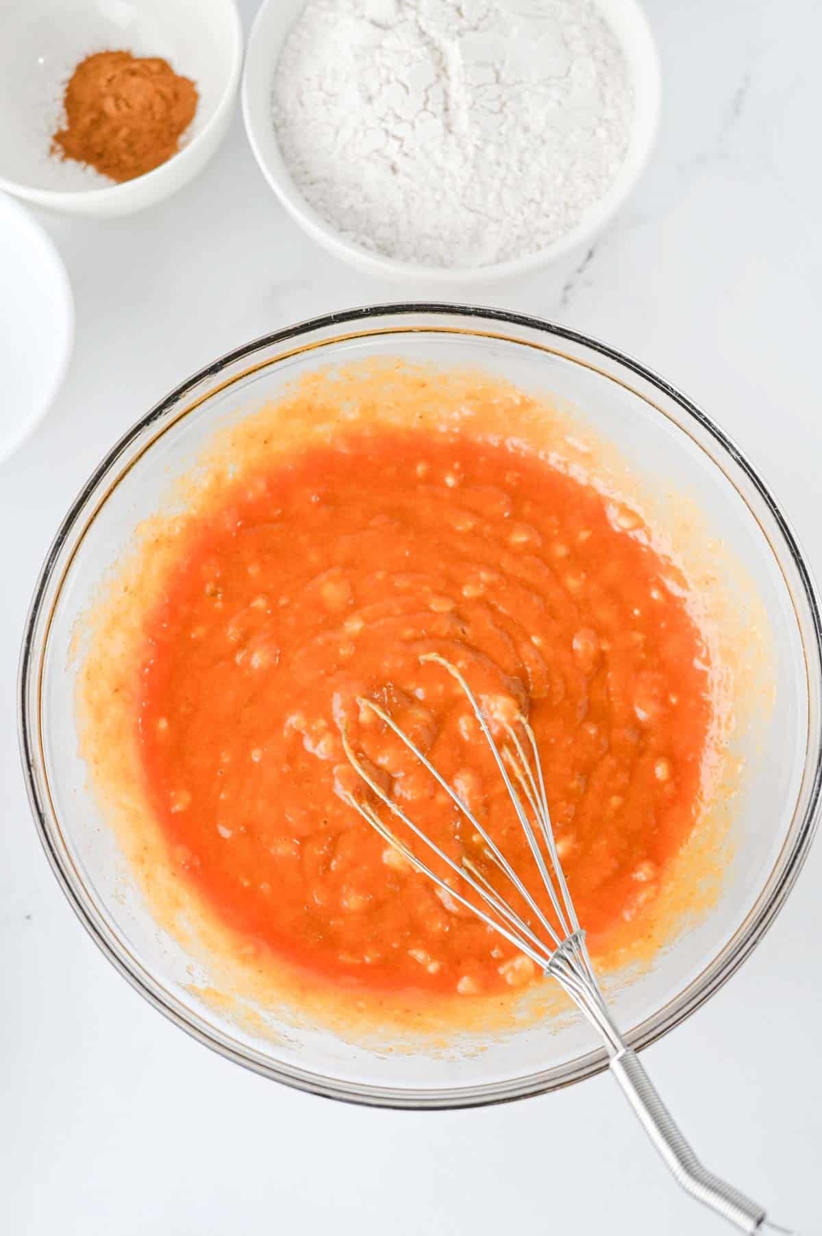 pumpkin puree and other wet ingredients combined in a glass mixning bowl