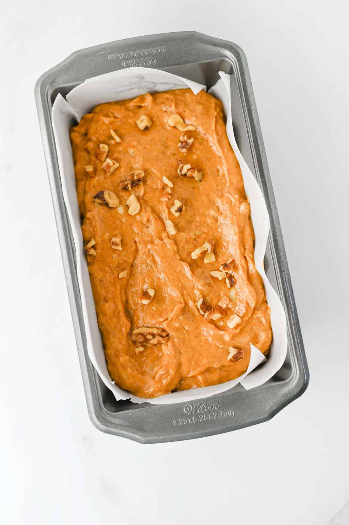 pumpkin banana bread batter in a parchment lined loaf pan with walnuts sprinkled on top