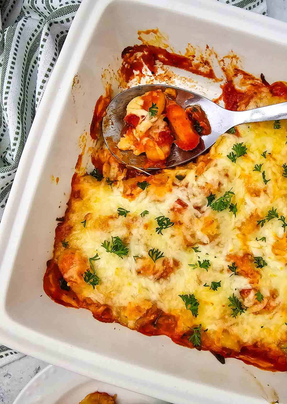 scooping baked gnocchi from a dish