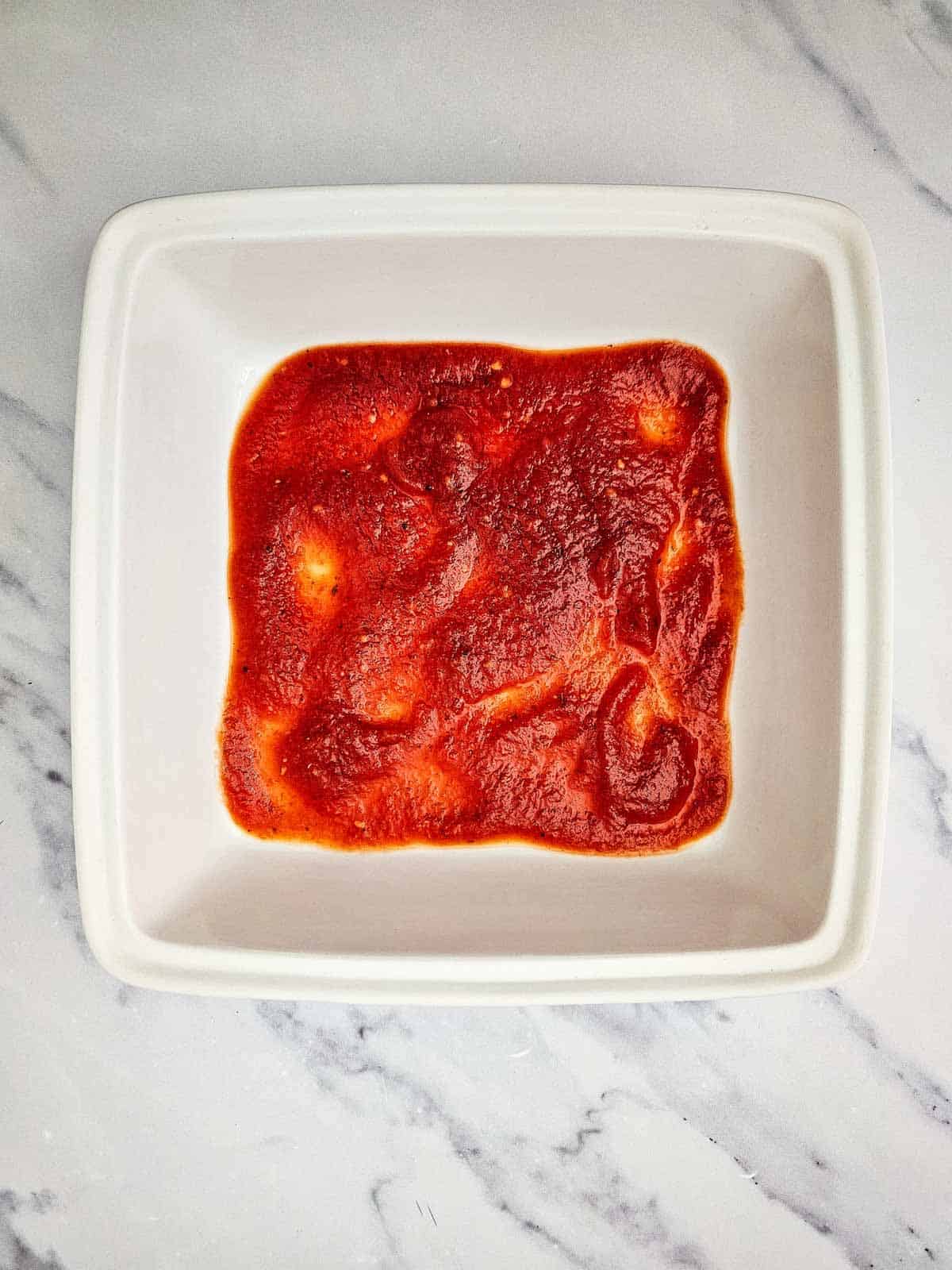 tomato sauce spread in the bottom of a baking dish