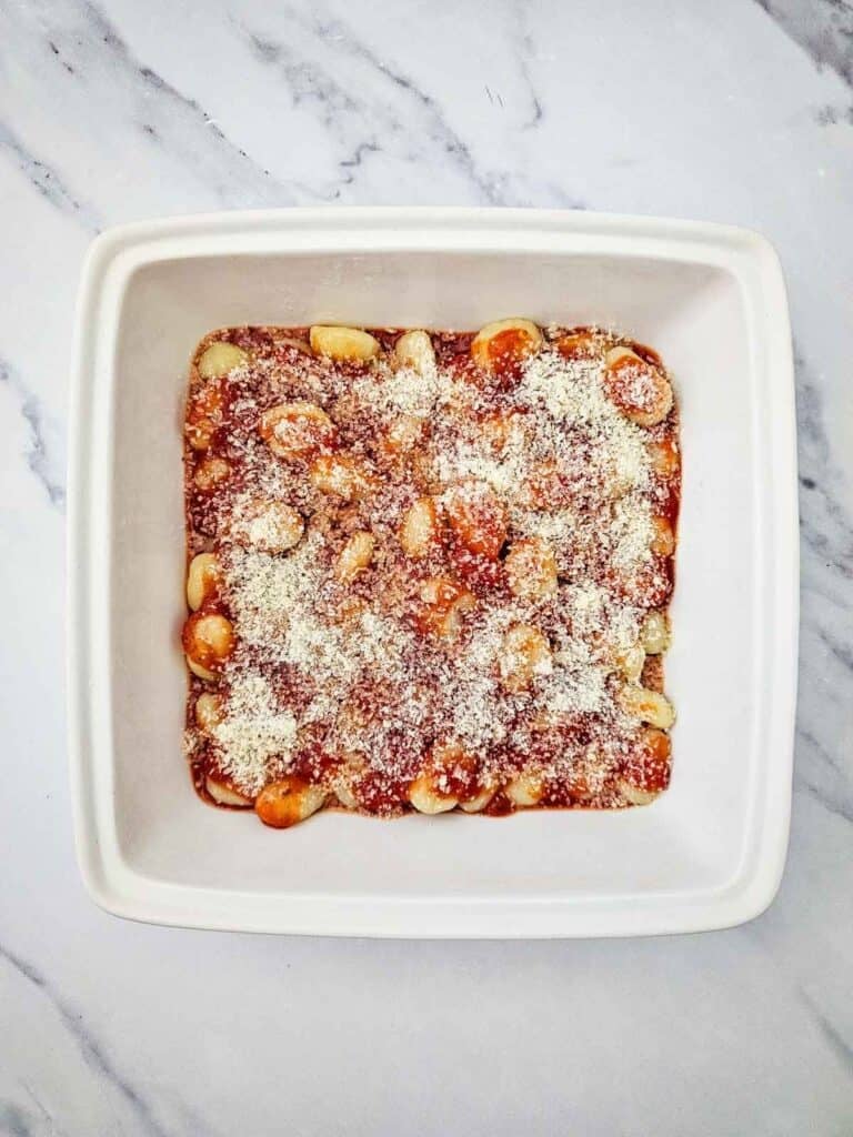 grated parmesan on top of gnocchi in a baking dish
