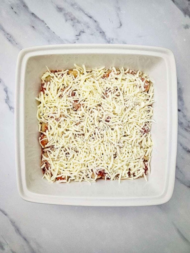 shredded cheese on top of gnocchi in a baking dish