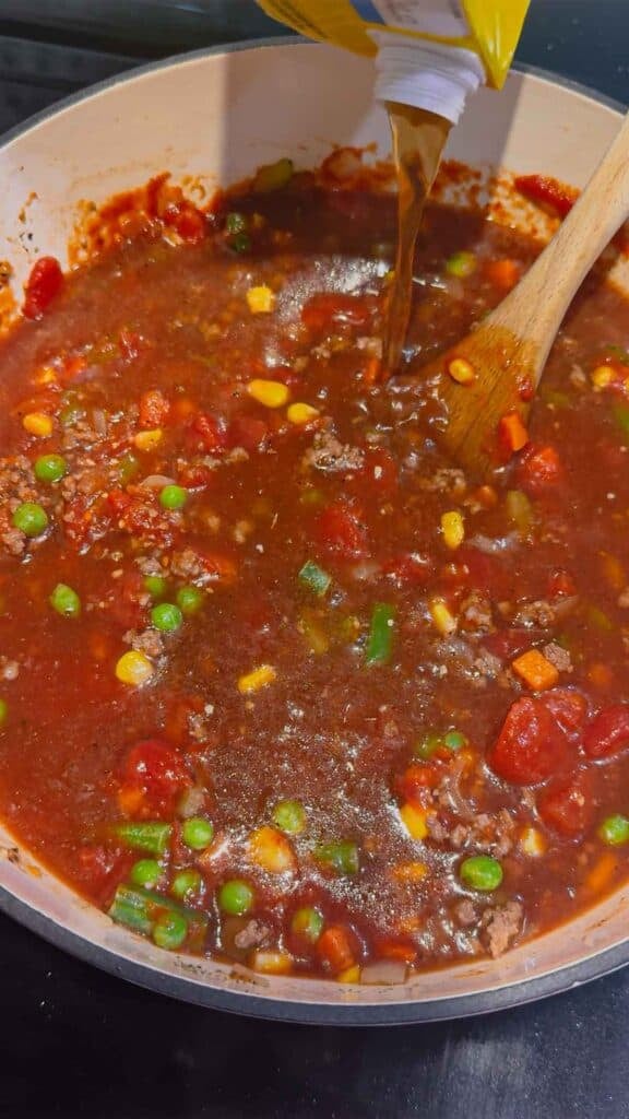 adding beef broth to beef vegetable soup in a pot