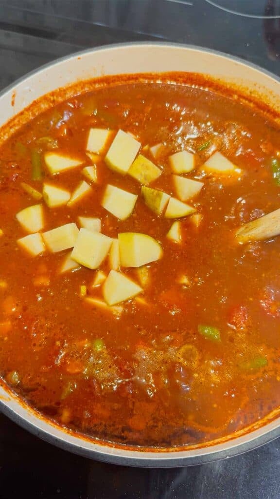 diced potatoes added to beef vegetable soup in a large pot