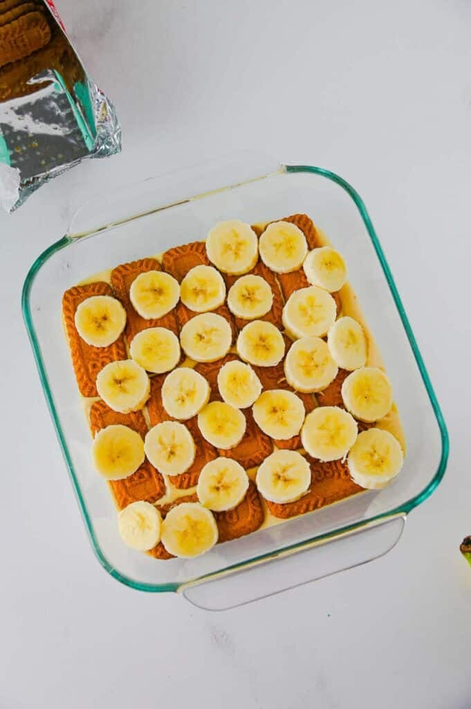 sliced banana pieces and biscoff cookies on top of pudding in a baking dish
