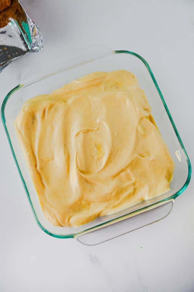 pudding mixture on top of banana slices and biscoff cookies in a baking dish