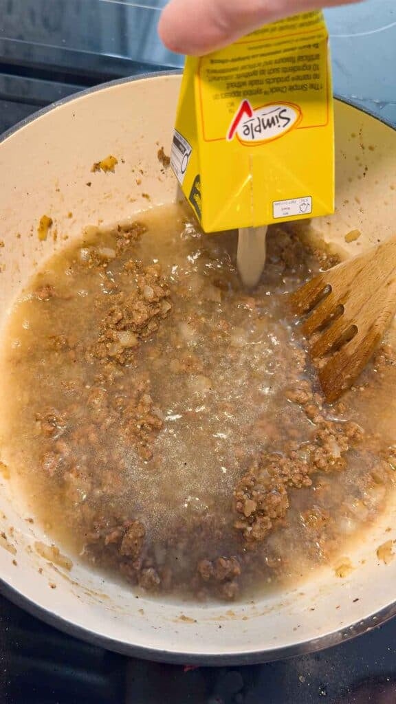 adding chicken broth to pot with ground beef and onions