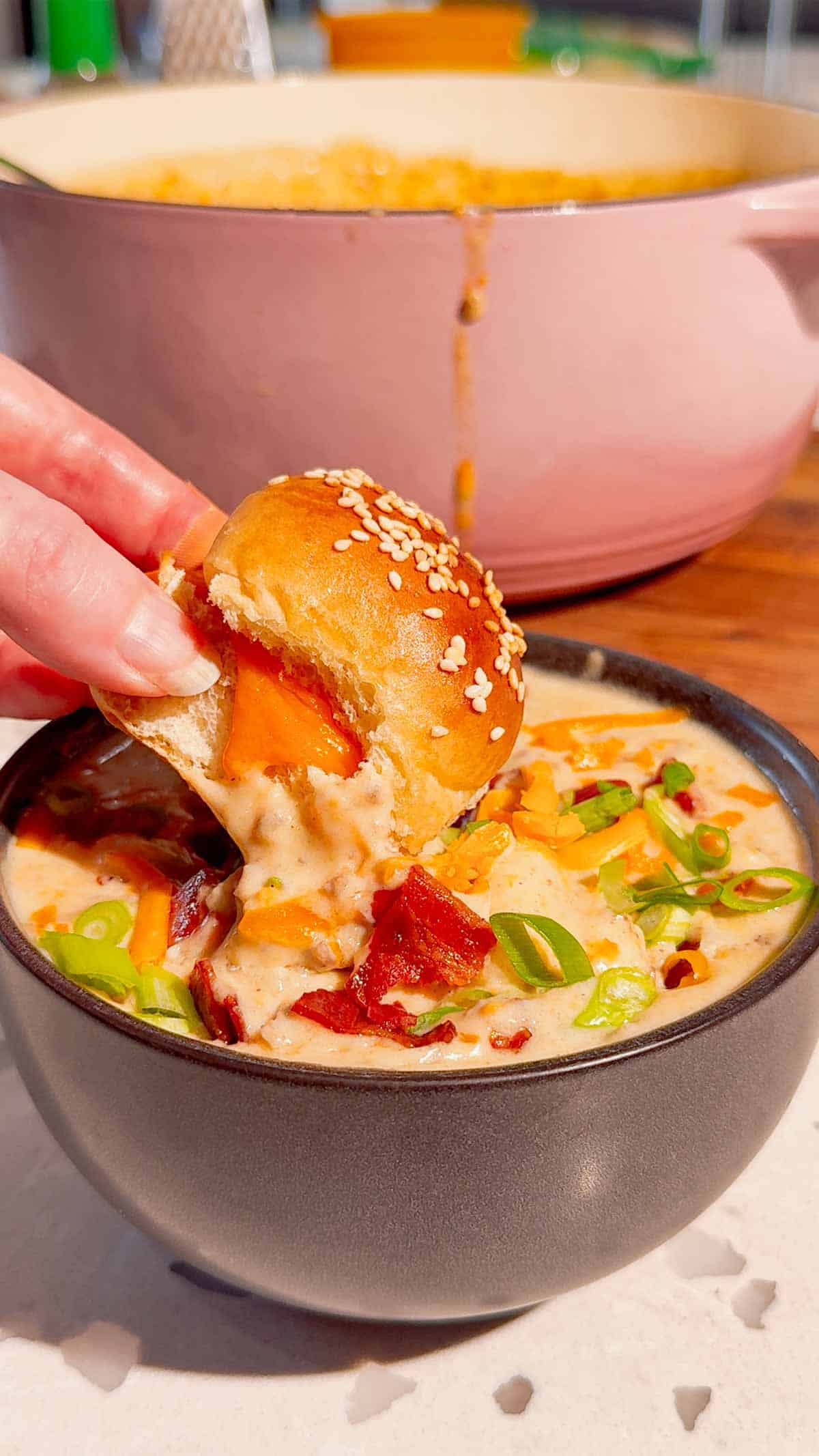 dipping small grilled cheese bun into cheeseburger gnocchi soup