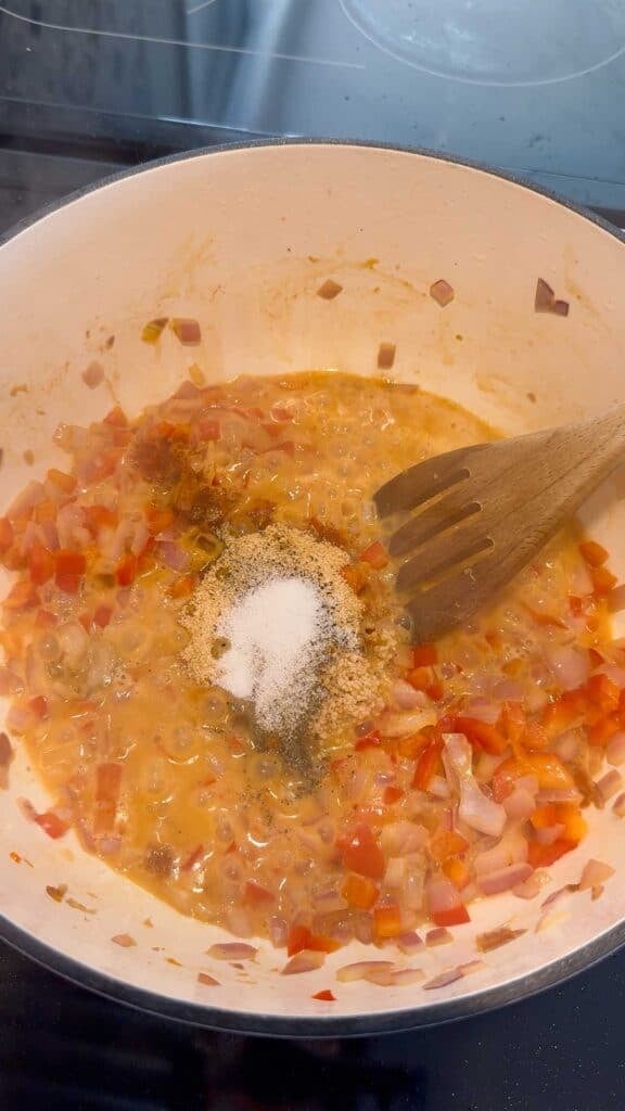 seasonings added to a pot with cooked diced red onions and red peppers