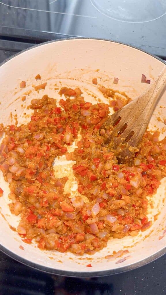 flour and butter being stirred with cooked red onions and peppers in a large pot