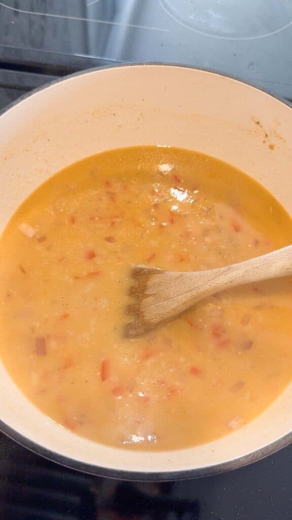 stirring chicken broth and cooked veggies in a large pot