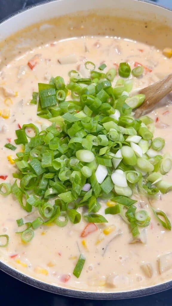 chopped green onions on top of chicken corn chowder in a pot