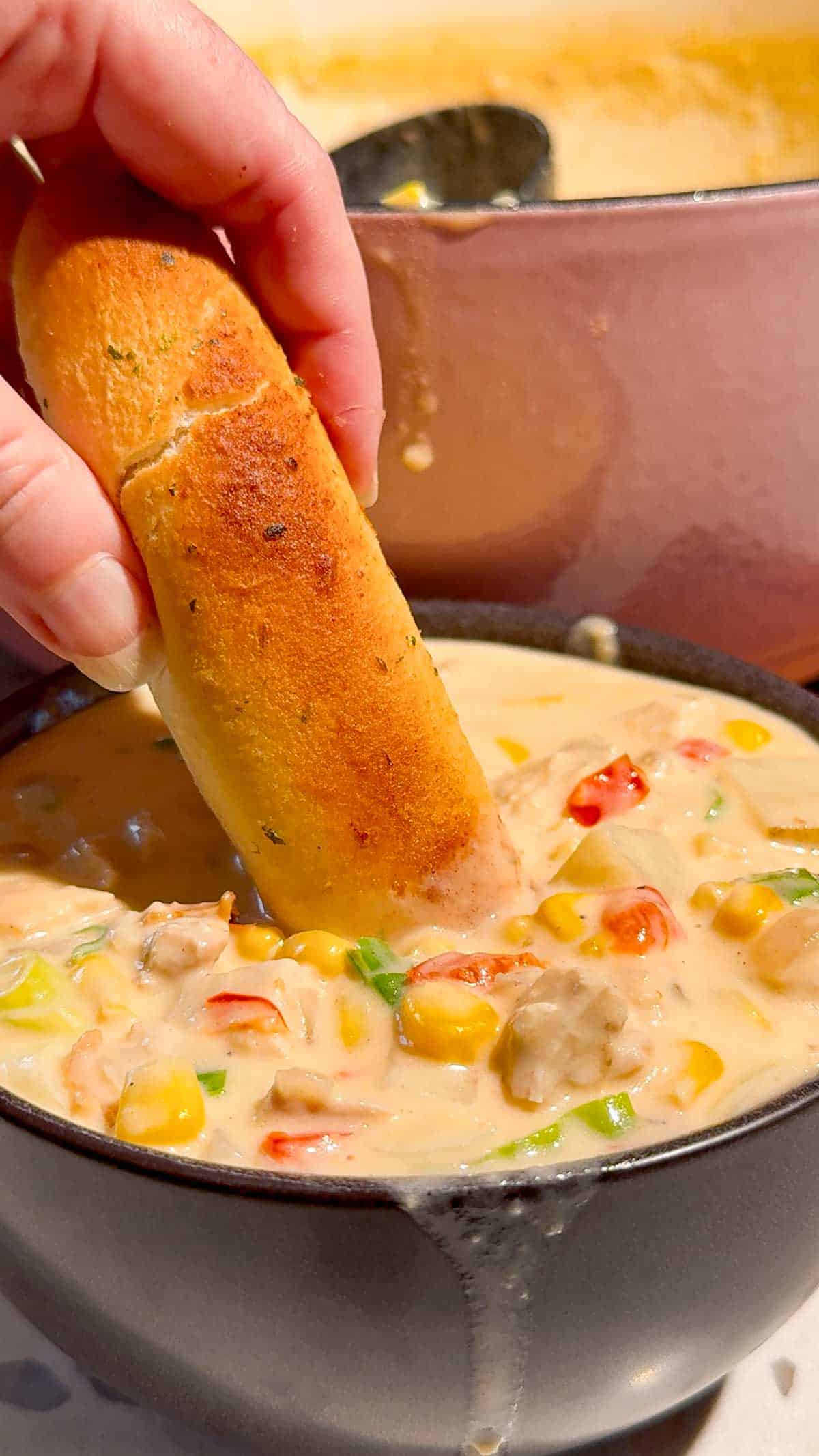 dipping breadstick into bowl of chicken corn chowder