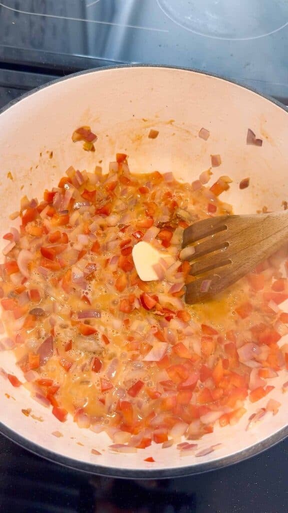 stirring melted butter with diced red onions and red bell peppers in a large pot