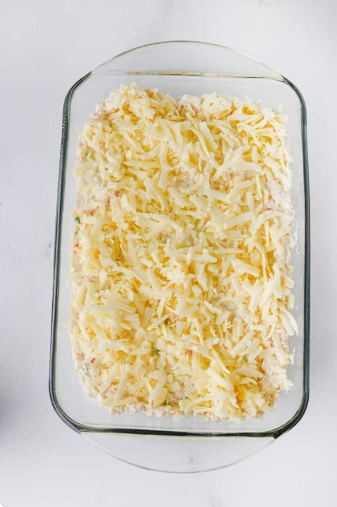shredded cheese on top of crab dip in a baking dish