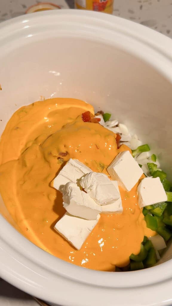 cubed cream cheese on top of salsa con queso, diced onions and peppers in a crock pot
