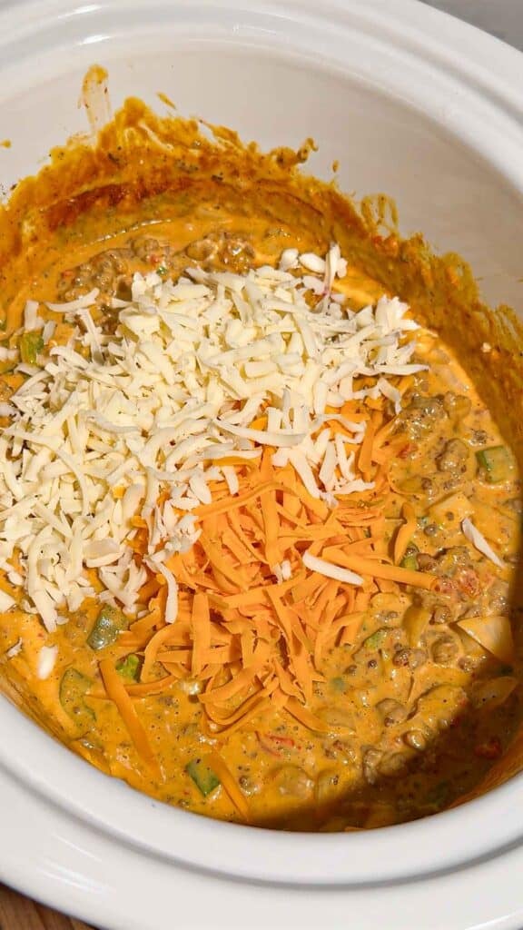 shredded mozzarella and cheddar cheese on top of nacho mixture in a slow cooker