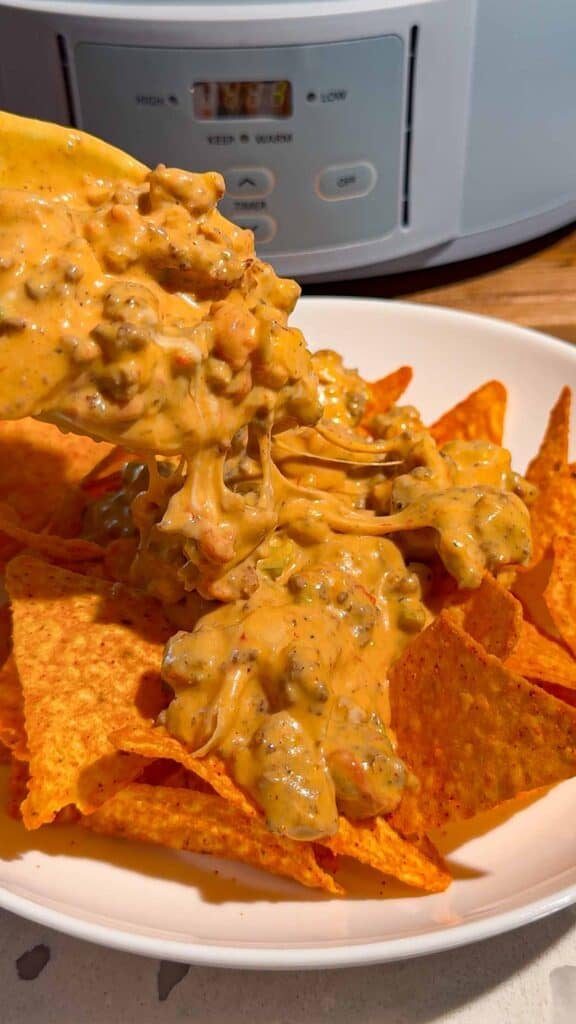 These Crock Pot Nachos are easy game day food, party appetizer or fun family dinner loaded with bold Tex-Mex flavor. This easy slow cooker nachos recipe combines seasoned ground beef, Italian sausage, onions, green peppers, Rotel, salsa con queso, cream cheese and shredded cheese for an extra creamy, meaty nacho topping. Spoon the cheesy Crock Pot nacho mixture over tortilla chips or Doritos, then add sour cream, guacamole, diced tomatoes, cilantro and jalapenos. If you need easy Crock Pot appetizers, slow cooker party food, football food ideas, Super Bowl snacks, nacho recipes or easy appetizers for a crowd, save this recipe. These loaded nachos are perfect for game day parties, potlucks, movie nights and casual entertaining when you want easy comfort food everyone will dig into!