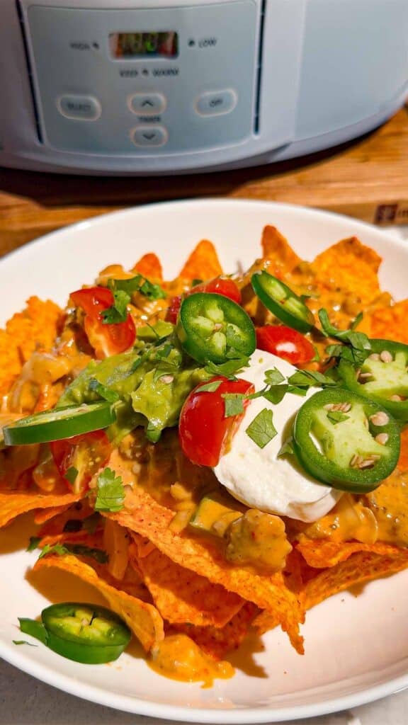 These Crock Pot Nachos are easy game day food, party appetizer or fun family dinner loaded with bold Tex-Mex flavor. This easy slow cooker nachos recipe combines seasoned ground beef, Italian sausage, onions, green peppers, Rotel, salsa con queso, cream cheese and shredded cheese for an extra creamy, meaty nacho topping. Spoon the cheesy Crock Pot nacho mixture over tortilla chips or Doritos, then add sour cream, guacamole, diced tomatoes, cilantro and jalapenos. If you need easy Crock Pot appetizers, slow cooker party food, football food ideas, Super Bowl snacks, nacho recipes or easy appetizers for a crowd, save this recipe. These loaded nachos are perfect for game day parties, potlucks, movie nights and casual entertaining when you want easy comfort food everyone will dig into!