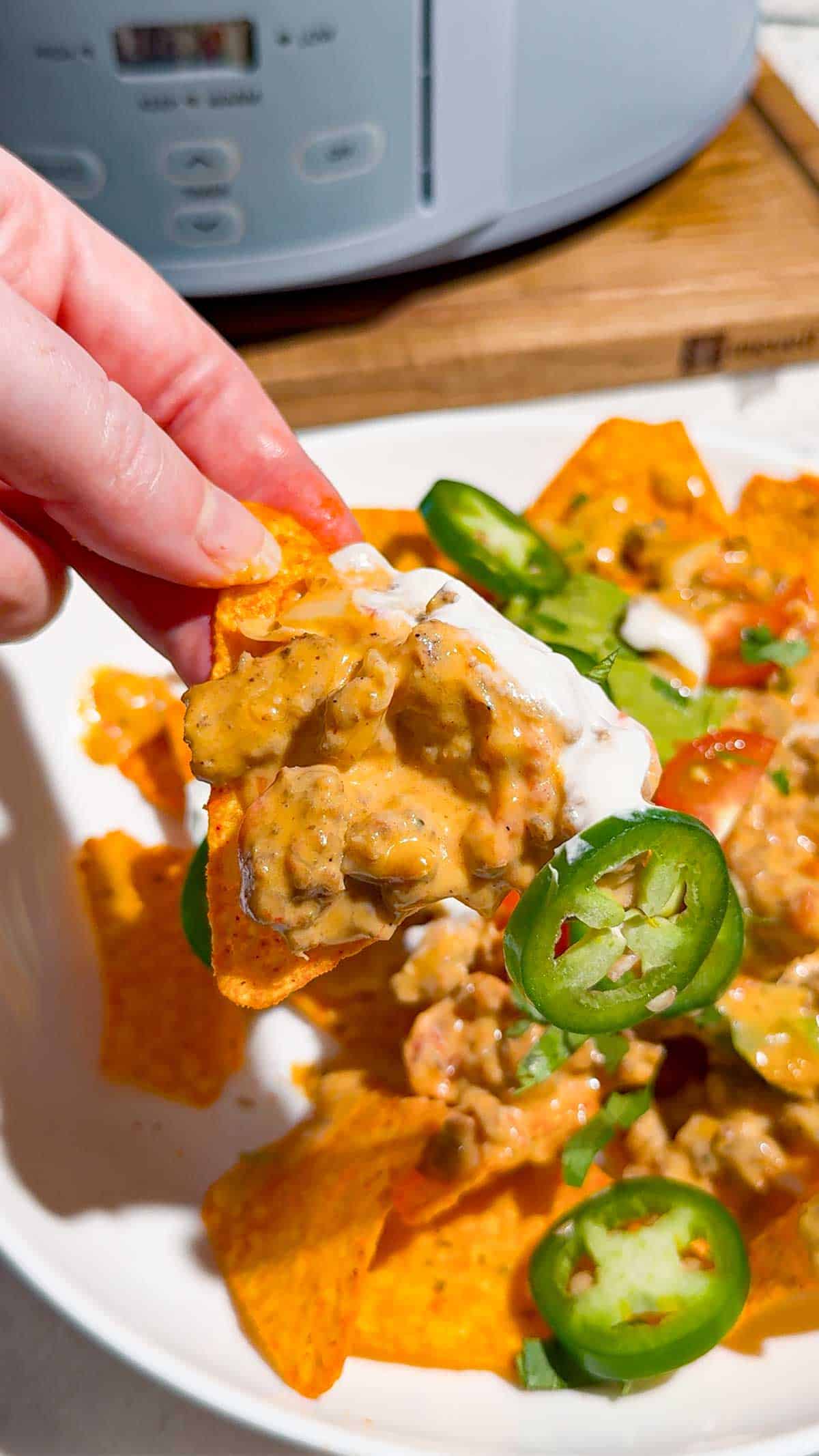 These Crock Pot Nachos are easy game day food, party appetizer or fun family dinner loaded with bold Tex-Mex flavor. This easy slow cooker nachos recipe combines seasoned ground beef, Italian sausage, onions, green peppers, Rotel, salsa con queso, cream cheese and shredded cheese for an extra creamy, meaty nacho topping. Spoon the cheesy Crock Pot nacho mixture over tortilla chips or Doritos, then add sour cream, guacamole, diced tomatoes, cilantro and jalapenos. If you need easy Crock Pot appetizers, slow cooker party food, football food ideas, Super Bowl snacks, nacho recipes or easy appetizers for a crowd, save this recipe. These loaded nachos are perfect for game day parties, potlucks, movie nights and casual entertaining when you want easy comfort food everyone will dig into!