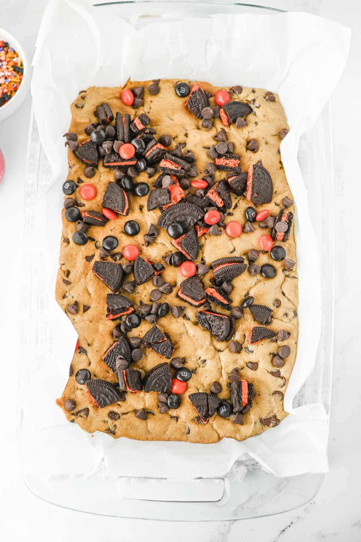 chopped oreos, chocolate chips and m&ms on top of baked cookie dough in a baking dish