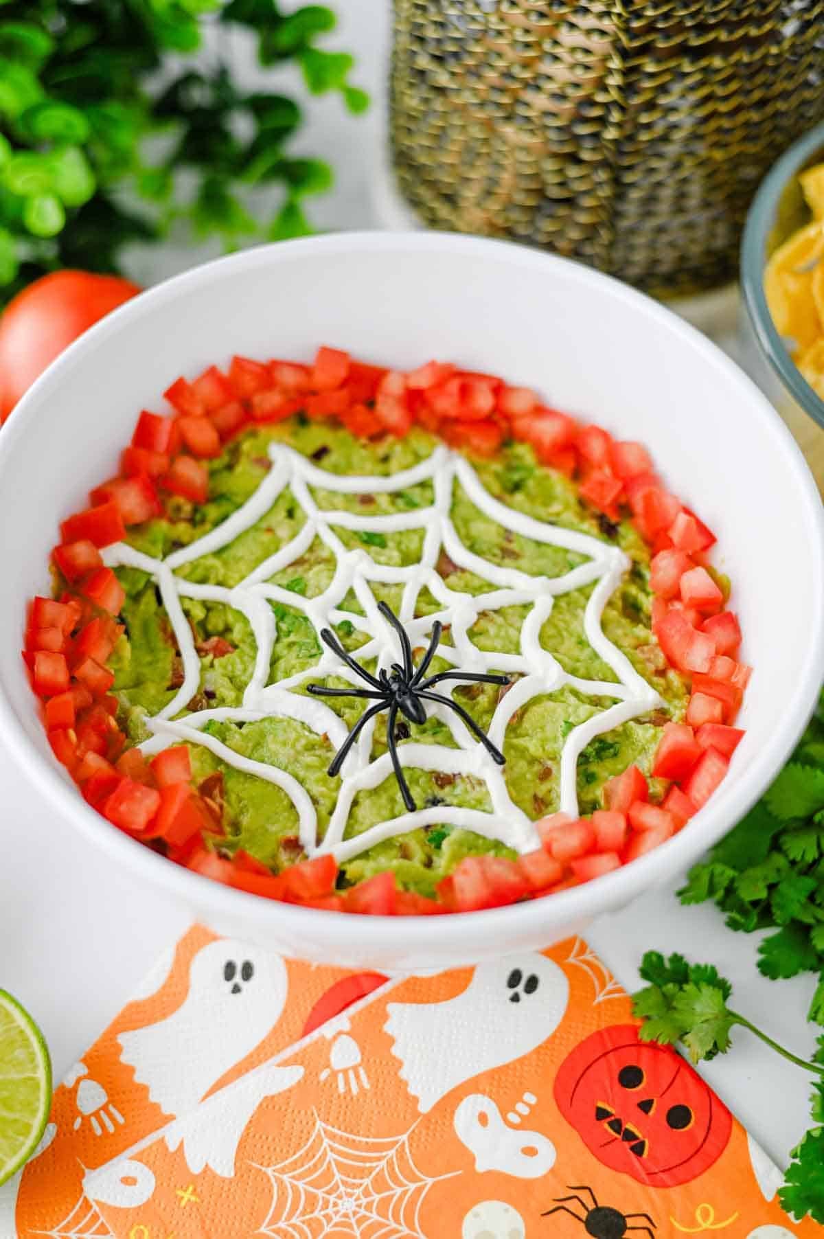 This Halloween Guacamole is the ultimate spooky appetizer for any spooky celebration! Creamy homemade guacamole with avocado, Roma tomatoes, red onion, fresh cilantro, and lime juice gets a festive makeover with an easy sour cream spider web on top. This Spider Web Guacamole is a fun Halloween dip that's ready in just 15 minutes and perfect with tortilla chips, crackers, or fresh veggies. If you need Easy Halloween Appetizers, Halloween Party Food, Halloween Dip Recipes, Spooky Halloween Food, Halloween Snacks for Kids, or Halloween Guacamole Ideas, this simple recipe belongs on your menu. Add diced tomatoes around the edge and a plastic spider for an extra creepy finish. It's an easy Halloween party appetizer that's fresh, colorful, delicious, and perfect for a Halloween snack table!