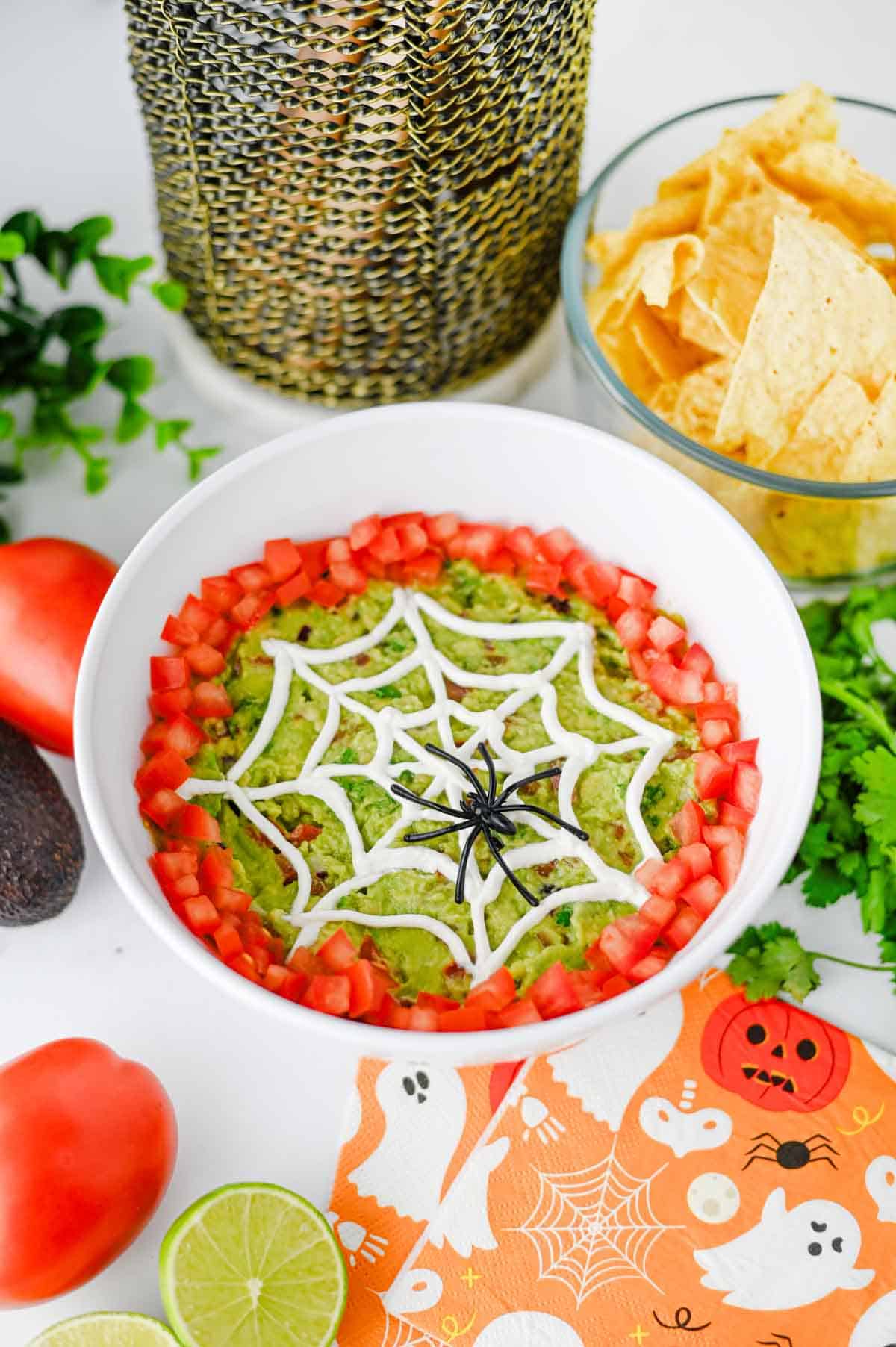 This Halloween Guacamole is the ultimate spooky appetizer for any spooky celebration! Creamy homemade guacamole with avocado, Roma tomatoes, red onion, fresh cilantro, and lime juice gets a festive makeover with an easy sour cream spider web on top. This Spider Web Guacamole is a fun Halloween dip that's ready in just 15 minutes and perfect with tortilla chips, crackers, or fresh veggies. If you need Easy Halloween Appetizers, Halloween Party Food, Halloween Dip Recipes, Spooky Halloween Food, Halloween Snacks for Kids, or Halloween Guacamole Ideas, this simple recipe belongs on your menu. Add diced tomatoes around the edge and a plastic spider for an extra creepy finish. It's an easy Halloween party appetizer that's fresh, colorful, delicious, and perfect for a Halloween snack table!