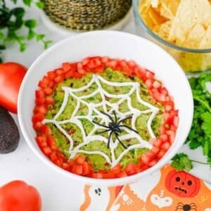 This Halloween Guacamole is the ultimate spooky appetizer for any spooky celebration! Creamy homemade guacamole with avocado, Roma tomatoes, red onion, fresh cilantro, and lime juice gets a festive makeover with an easy sour cream spider web on top. This Spider Web Guacamole is a fun Halloween dip that's ready in just 15 minutes and perfect with tortilla chips, crackers, or fresh veggies. If you need Easy Halloween Appetizers, Halloween Party Food, Halloween Dip Recipes, Spooky Halloween Food, Halloween Snacks for Kids, or Halloween Guacamole Ideas, this simple recipe belongs on your menu. Add diced tomatoes around the edge and a plastic spider for an extra creepy finish. It's an easy Halloween party appetizer that's fresh, colorful, delicious, and perfect for a Halloween snack table!