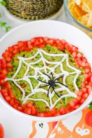This Halloween Guacamole is the ultimate spooky appetizer for any spooky celebration! Creamy homemade guacamole with avocado, Roma tomatoes, red onion, fresh cilantro, and lime juice gets a festive makeover with an easy sour cream spider web on top. This Spider Web Guacamole is a fun Halloween dip that's ready in just 15 minutes and perfect with tortilla chips, crackers, or fresh veggies. If you need Easy Halloween Appetizers, Halloween Party Food, Halloween Dip Recipes, Spooky Halloween Food, Halloween Snacks for Kids, or Halloween Guacamole Ideas, this simple recipe belongs on your menu. Add diced tomatoes around the edge and a plastic spider for an extra creepy finish. It's an easy Halloween party appetizer that's fresh, colorful, delicious, and perfect for a Halloween snack table!