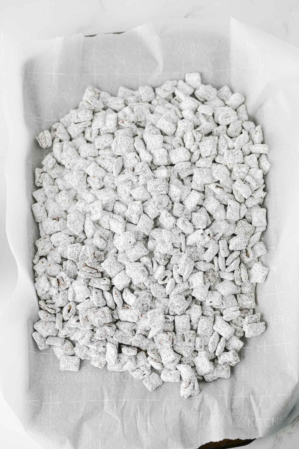 powdered sugar and chocolate coated cereal on a parchment lined baking sheet