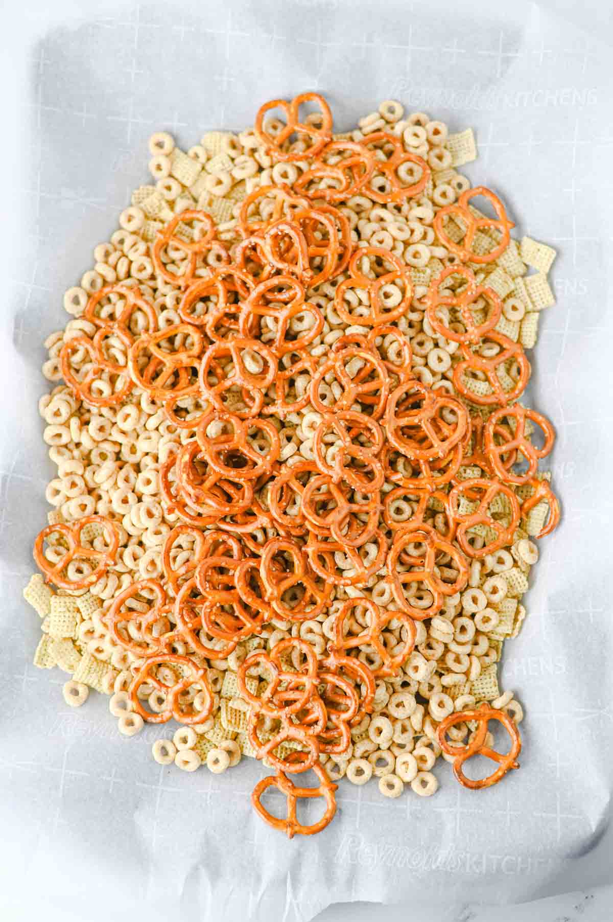 cheerios, chex cereal and pretzels on a parchment lined baking sheet