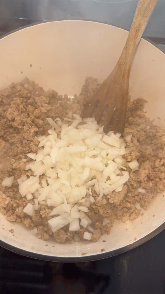 diced onions on top of cooked ground meat in a large pot