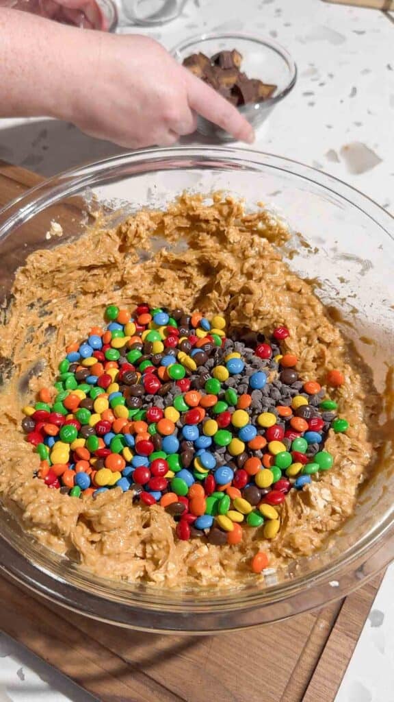 mini M&Ms and mini chocolate chips on top of peanut butter mixture in a glass bowl