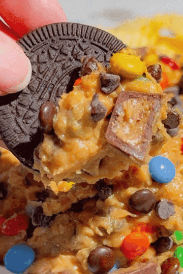 This Monster Cookie Dough Dip is an easy no bake dessert dip loaded with crunchy peanut butter, brown sugar, quick oats, mini chocolate chips, mini M&Ms and chopped Reese’s peanut butter cups. It’s the perfect sweet party dip for holidays, birthdays, game day, potlucks, movie nights and easy entertaining. Serve this creamy peanut butter cookie dough dip with graham crackers, pretzels, vanilla wafers, cookies or apple slices for a fun dessert board everyone will dig into. If you love monster cookies, peanut butter desserts, cookie dough dip recipes, M&M desserts, Reese’s desserts and quick no bake treats, this 15 minute dessert dip is a must try for your next party or family gathering.