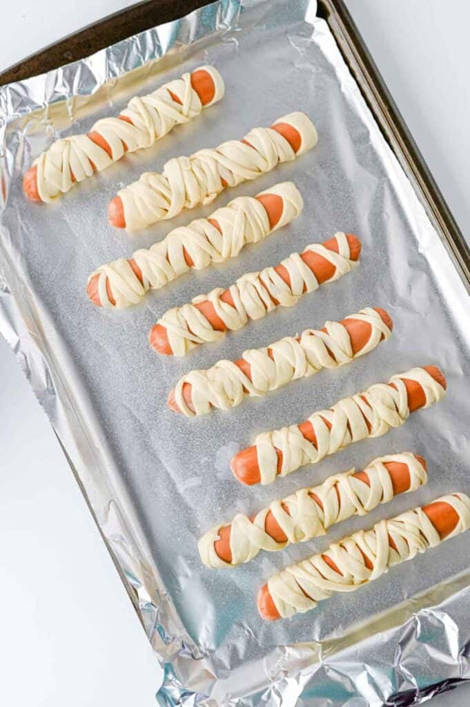mummy hot dogs on a foil lined baking sheet before baking