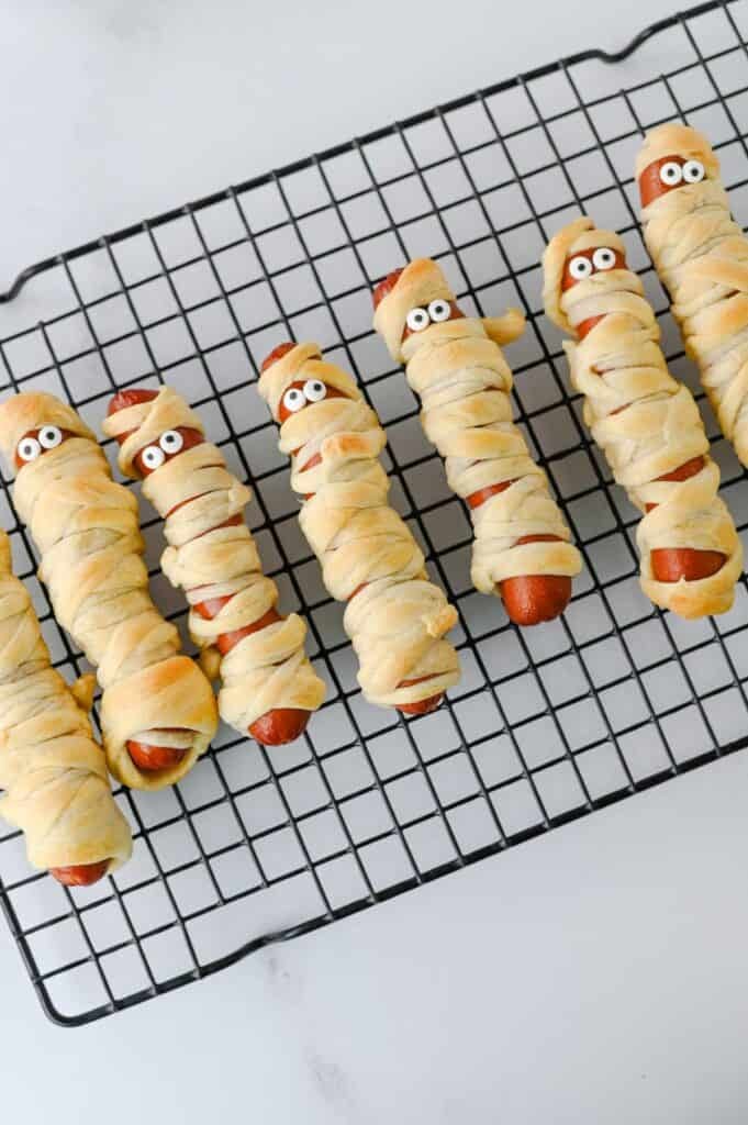 These Mummy Hot Dogs are the perfect easy Halloween dinner, spooky party snack, or kid-friendly Halloween appetizer! Made with hot dogs wrapped in flaky crescent roll dough, these adorable Crescent Roll Mummy Hot Dogs are quick to prep and baked until golden. Add candy eyes for a fun finishing touch, then serve with ketchup and mustard for dipping. If you need Easy Halloween Food Ideas, Halloween Party Food For Kids, Halloween Hot Dog Ideas, Halloween Finger Foods, Spooky Halloween Snacks, or Halloween Dinner Ideas For Kids, this simple recipe is a must-try. These Halloween Mummy Dogs are great for Halloween parties, movie nights, or a festive family dinner. Save this Mummy Hot Dogs Recipe for an easy Halloween snack that's cute, delicious, and made with a few simple ingredients!