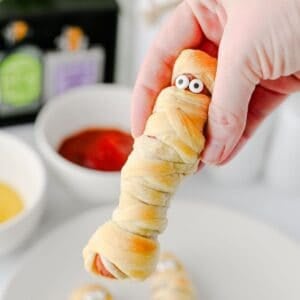 These Mummy Hot Dogs are the perfect easy Halloween dinner, spooky party snack, or kid-friendly Halloween appetizer! Made with hot dogs wrapped in flaky crescent roll dough, these adorable Crescent Roll Mummy Hot Dogs are quick to prep and baked until golden. Add candy eyes for a fun finishing touch, then serve with ketchup and mustard for dipping. If you need Easy Halloween Food Ideas, Halloween Party Food For Kids, Halloween Hot Dog Ideas, Halloween Finger Foods, Spooky Halloween Snacks, or Halloween Dinner Ideas For Kids, this simple recipe is a must-try. These Halloween Mummy Dogs are great for Halloween parties, movie nights, or a festive family dinner. Save this Mummy Hot Dogs Recipe for an easy Halloween snack that's cute, delicious, and made with a few simple ingredients!
