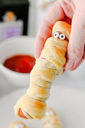 These Mummy Hot Dogs are the perfect easy Halloween dinner, spooky party snack, or kid-friendly Halloween appetizer! Made with hot dogs wrapped in flaky crescent roll dough, these adorable Crescent Roll Mummy Hot Dogs are quick to prep and baked until golden. Add candy eyes for a fun finishing touch, then serve with ketchup and mustard for dipping. If you need Easy Halloween Food Ideas, Halloween Party Food For Kids, Halloween Hot Dog Ideas, Halloween Finger Foods, Spooky Halloween Snacks, or Halloween Dinner Ideas For Kids, this simple recipe is a must-try. These Halloween Mummy Dogs are great for Halloween parties, movie nights, or a festive family dinner. Save this Mummy Hot Dogs Recipe for an easy Halloween snack that's cute, delicious, and made with a few simple ingredients!